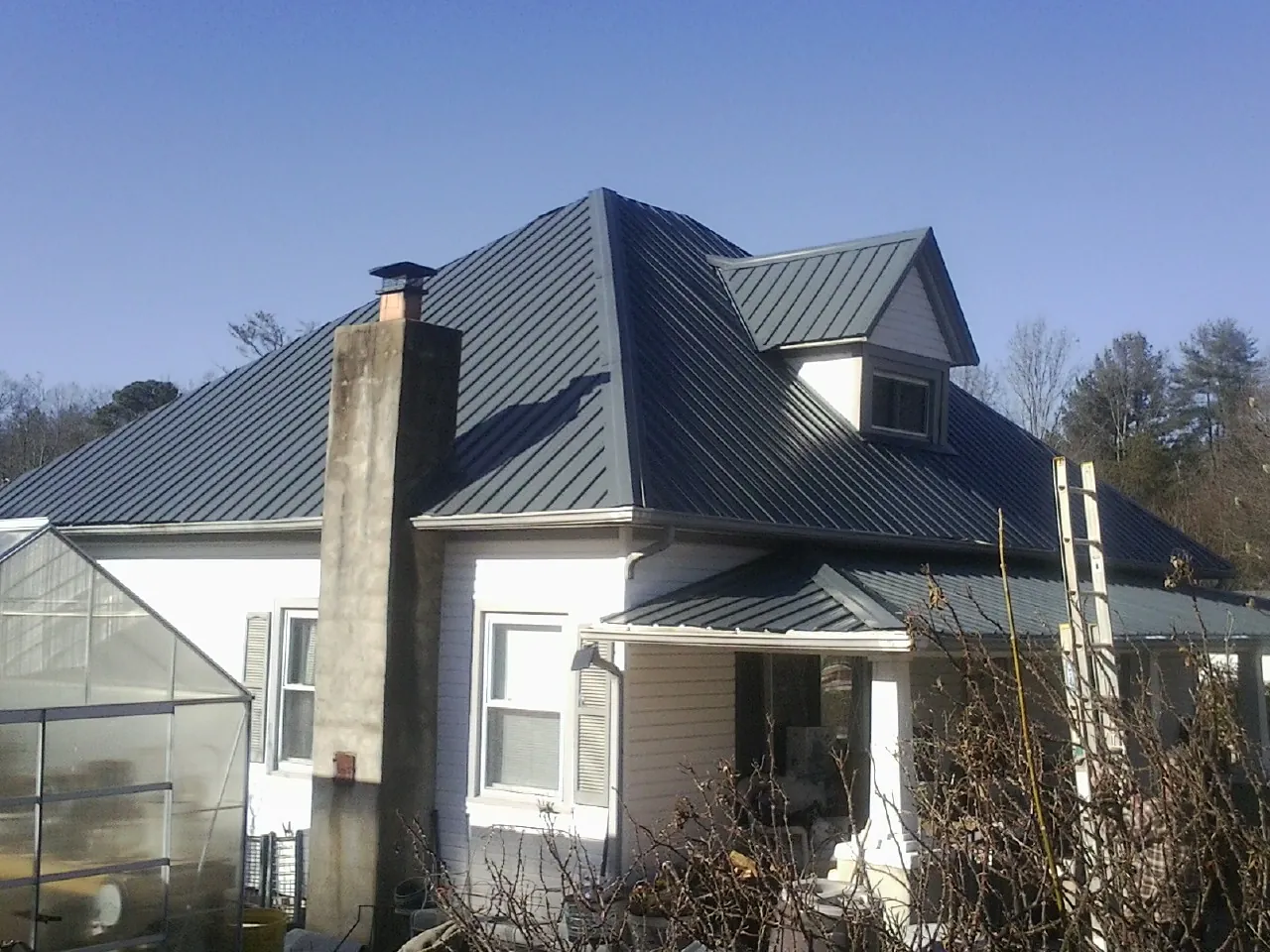 Dark blue standing seam metal roof on a white farmhouse with dormer — Slate & Tile Roof Repair by Roofing Brothers in Surfside