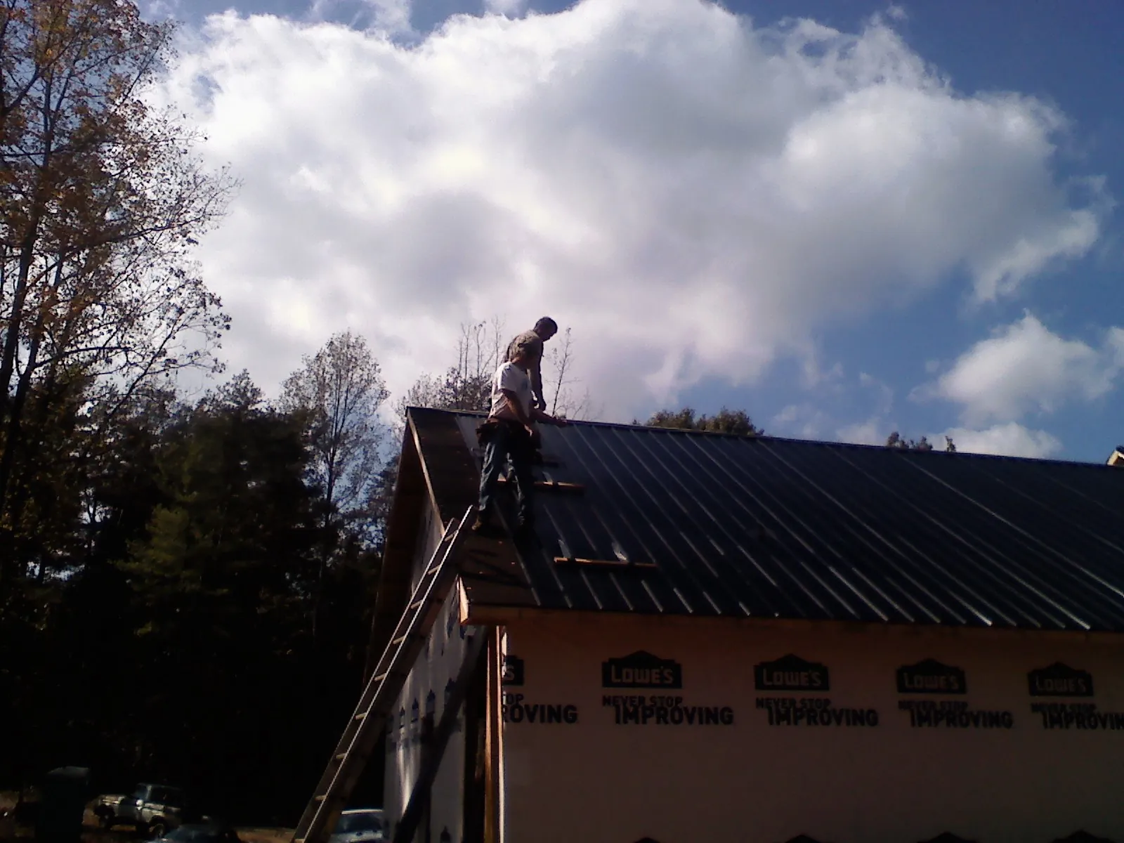 Roofer fastening dark metal panels high against a cloudy sky, from a Roof Inspection job in Surfside