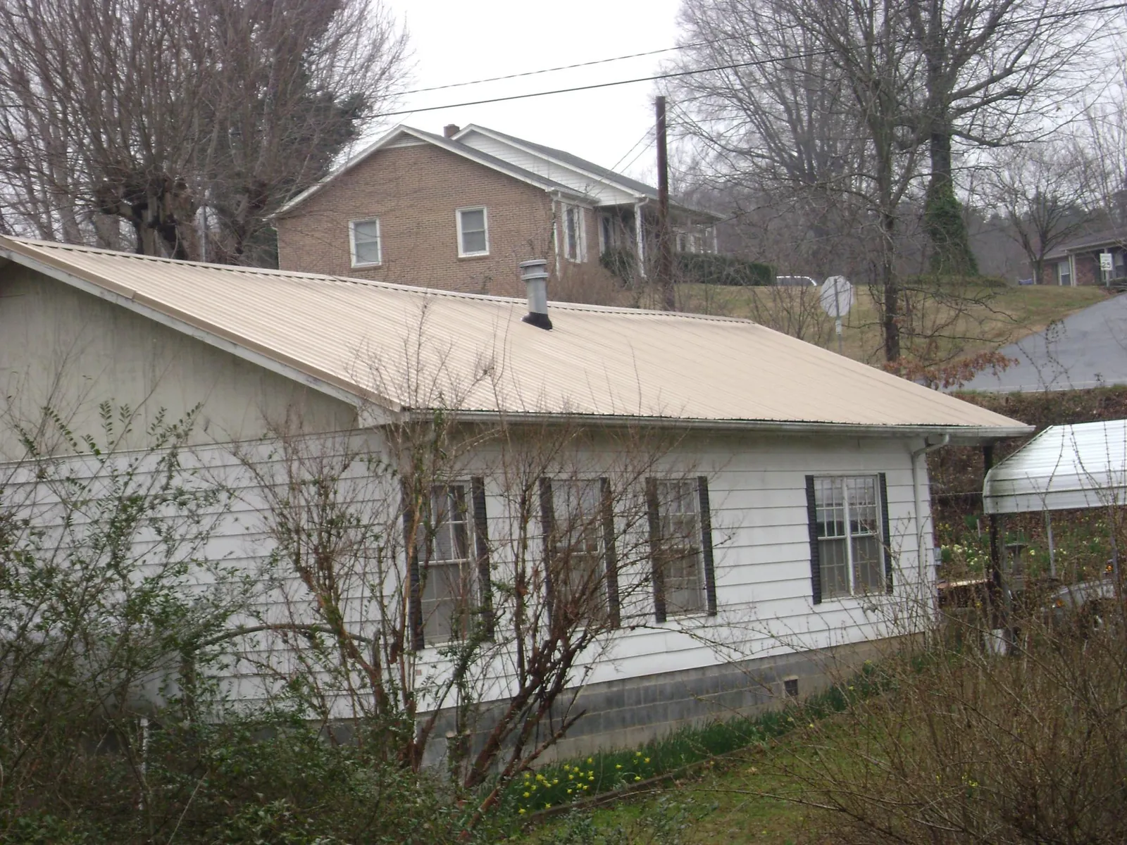 Tan metal roof on a white sided house set into a hillside — Commercial Roofing by Roofing Brothers in Surfside